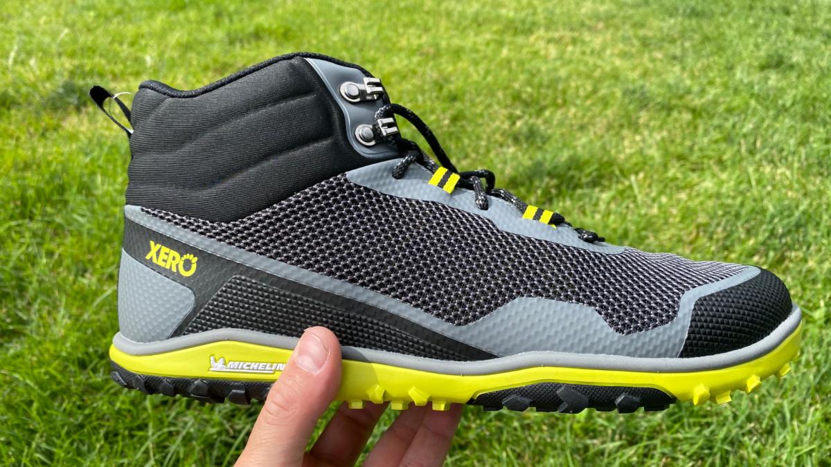 xero-shoes-scrambler-mid-grey-lime-green-hand-holding-side-view-grass-background